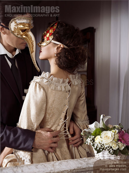 Sensual portrait of a couple in vintage Venetian carnival costumes. Man unlacing corset dress back of a beautiful woman. Stock photo of Sensual portrait of a couple in vintage Venetian carnival costumes. Man unlacing corset dress back of a beautiful woman. Buy commercial use license at MaximImages