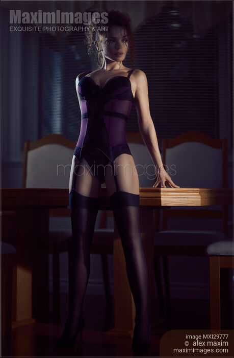 Stock photo of Sensual portrait of a woman in a corset and stockings leaning against a table in a bold pose Buy commercial use license at MaximImages