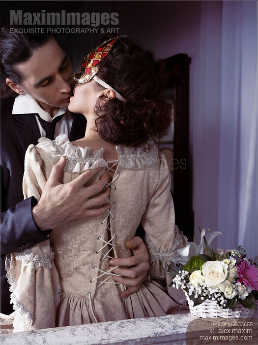 Sensual romantic portrait of a kissing couple. Elegant man unlacing corset dress back of a woman in Venetian carnival mask. Stock photo of Sensual romantic portrait of a kissing couple. Elegant man unlacing corset dress back of a woman in Venetian carnival mask. Buy commercial use license at MaximImages