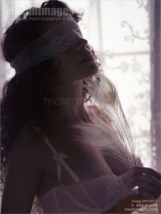 Stock photo of Sexy young woman face blindfolded with a lace touching her neck with a white peacock feather Buy commercial use license at MaximImages