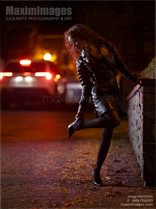 Sexy young woman in black leather coat fixing a high heel shoe on night city street in car lights Stock photo of Sexy young woman in black leather coat fixing a high heel shoe on night city street in car lights Buy commercial use license at MaximImages