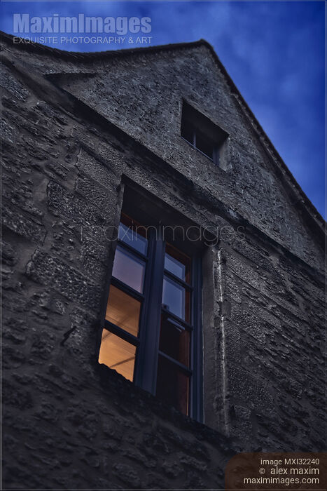 Stock photo of Shut window of an old European house at night illuminated from inside with dim light Buy commercial use license at MaximImages