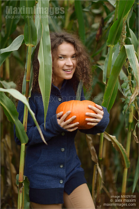 Stock photo of Smiling young woman with a pumpkin at a farm in fall Buy commercial use license at MaximImages