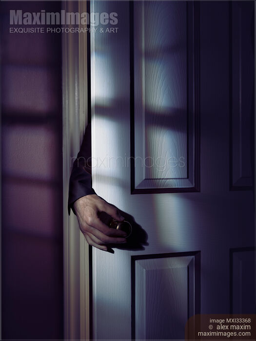 Stock photo of Spooky male hand reaching for a door handle from behind a room door at night Buy commercial use license at MaximImages