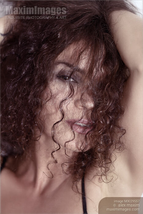 Stock photo of Sultry beauty face portrait of young woman looking through her long curly brown hair Buy commercial use license at MaximImages