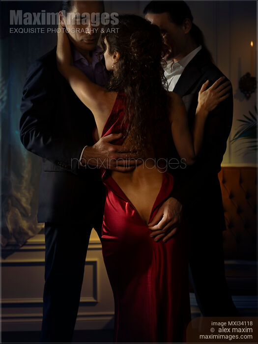 Stock photo of Two elegant men seducing a beautiful classy lady in red evening dress. Ménage a trois, suggestive romantic photo. Buy commercial use license at MaximImages