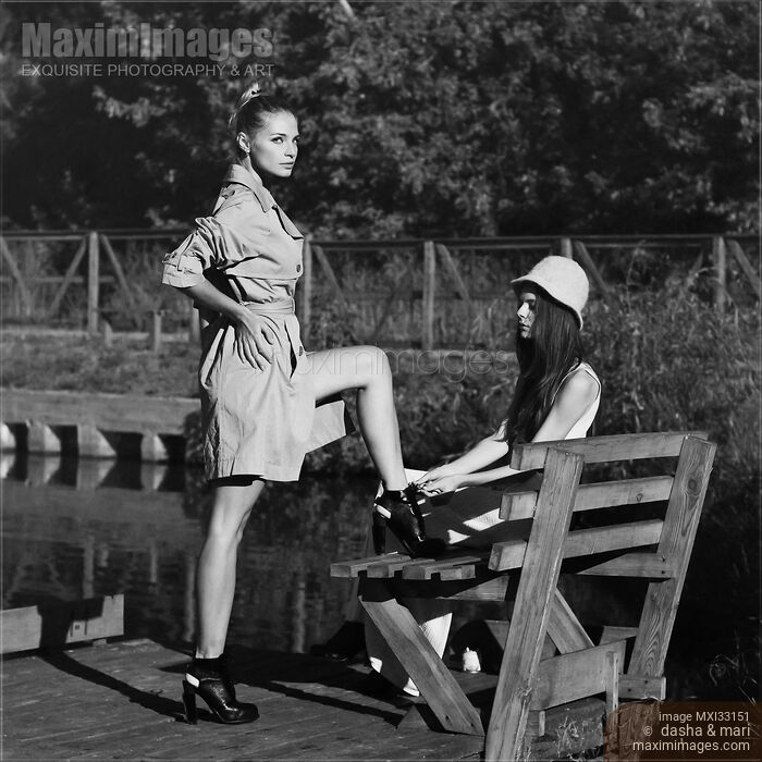 Two fashionable young women are dressing up before going out sitting on a bench by the river Stock photo of Two fashionable young women are dressing up before going out sitting on a bench by the river Buy commercial use license at MaximImages