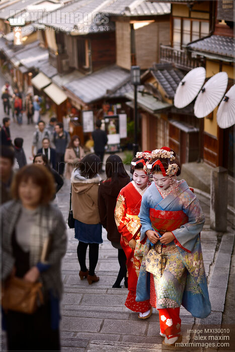 Stock photo of Two Maiko Geisha apprentices in kimono walking on streets among people in Kyoto Buy commercial use license at MaximImages