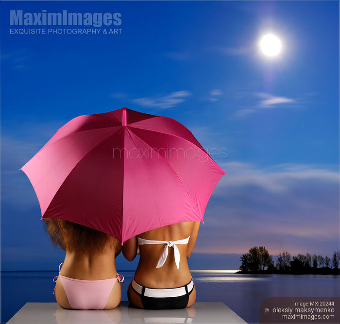 Stock photo of Two Women sitting together on a shore under umbrella Buy commercial use license at MaximImages