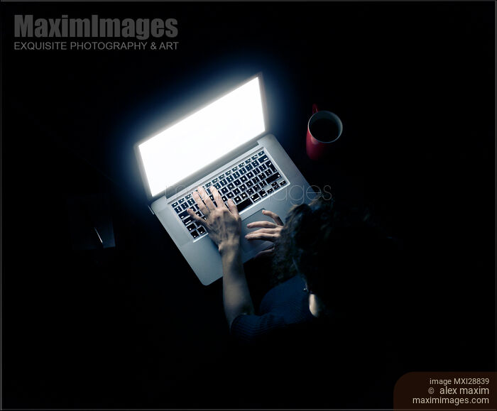 Woman at a desk in darkness with a glowing laptop computer screen Stock photo of Woman at a desk in darkness with a glowing laptop computer screen Buy commercial use license at MaximImages