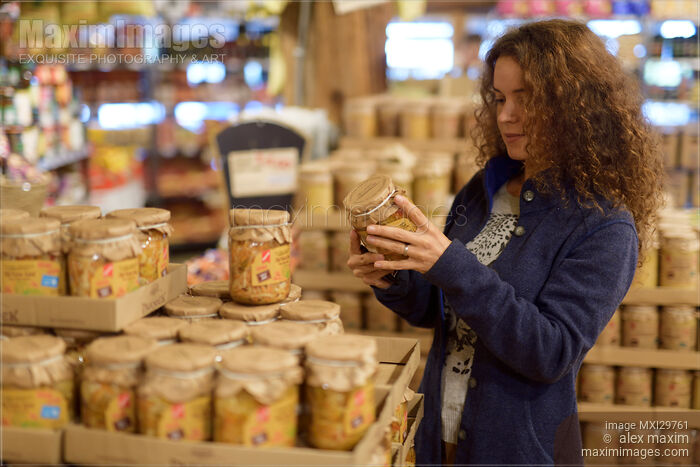 Stock photo of Woman at a grocery store looking at canned food products Buy commercial use license at MaximImages