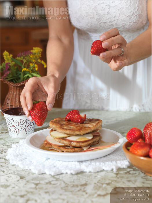 Stock photo of Woman decorating pancakes with strawberries Buy commercial use license at MaximImages