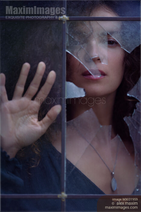 Stock photo of Woman face looking from behind a broken window glass drama and mystery concept Buy commercial use license at MaximImages