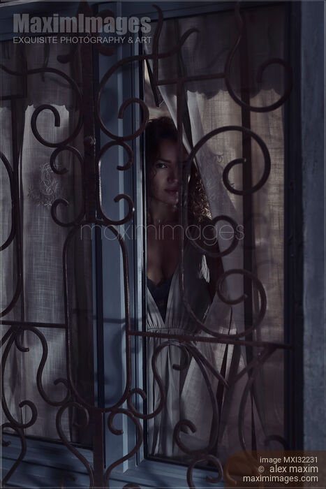 Stock photo of Woman face looking outside through a window behind grates at night Buy commercial use license at MaximImages