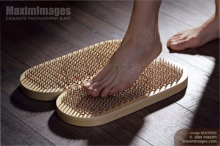 Stock photo of Woman foot stepping on Sadhu Board Yogic board of sharp metal nails Buy commercial use license at MaximImages