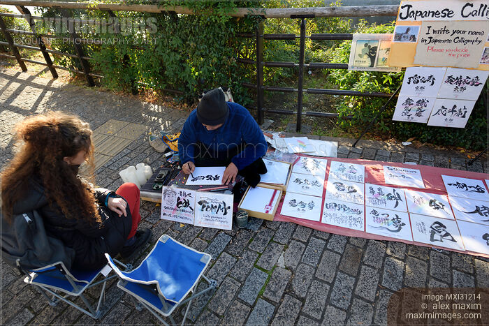 Stock photo of Woman gets her name written in Japanese characters by a street artist calligrapher Buy commercial use license at MaximImages