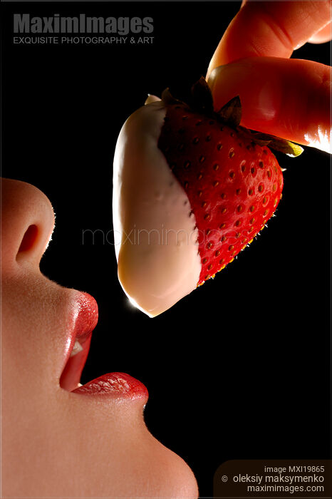 Stock photo of Woman holding strawberry in cream at her mouth Buy commercial use license at MaximImages