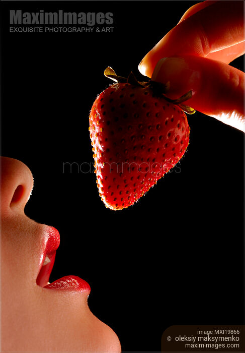 Stock photo of Woman holding strawberry near mouth Buy commercial use license at MaximImages