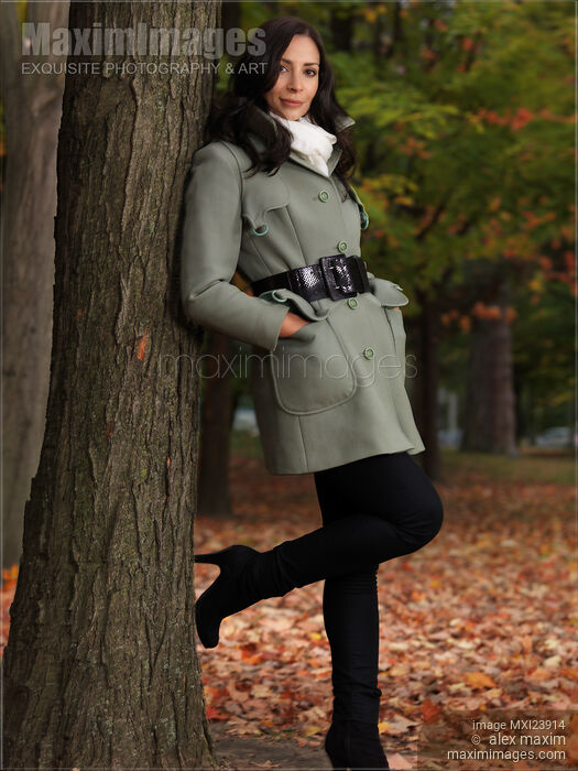 Stock photo of Woman in a Green Coat Leaning Against a Tree Buy commercial use license at MaximImages