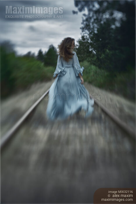 Woman in a long dress walking along railroad tracks in the wind Stock photo of Woman in a long dress walking along railroad tracks in the wind Buy commercial use license at MaximImages