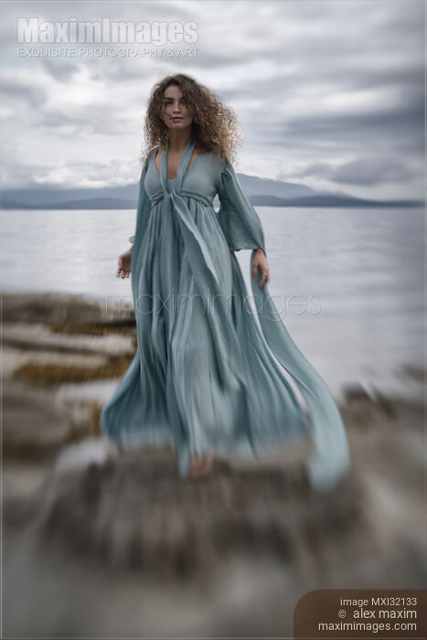 Woman in a long dress walking along the sea shore in a dramatic stormy scenery Stock photo of Woman in a long dress walking along the sea shore in a dramatic stormy scenery Buy commercial use license at MaximImages