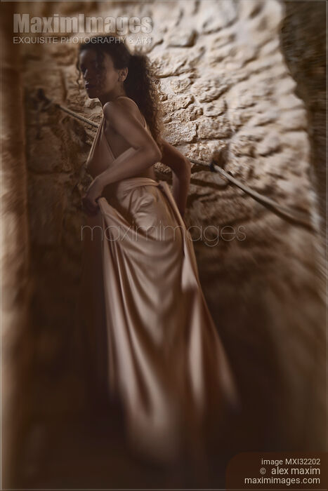 Stock photo of Woman in a long gown walking up a dark spiral staircase of a French house looking back Buy commercial use license at MaximImages