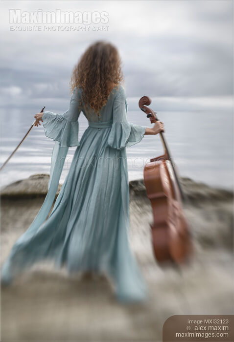 Woman in a long vintage dress standing gracefully by the ocean shore with a cello and a bow Stock photo of Woman in a long vintage dress standing gracefully by the ocean shore with a cello and a bow Buy commercial use license at MaximImages