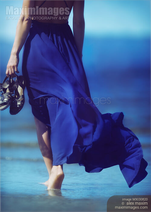 Woman in blue summer dress blowing in the wind walking barefoot on ocean beach sand Stock photo of Woman in blue summer dress blowing in the wind walking barefoot on ocean beach sand Buy commercial use license at MaximImages