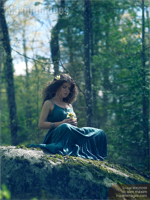 Stock photo of Woman in green dress sitting on rocks in the nature with a flower in her hands Buy commercial use license at MaximImages