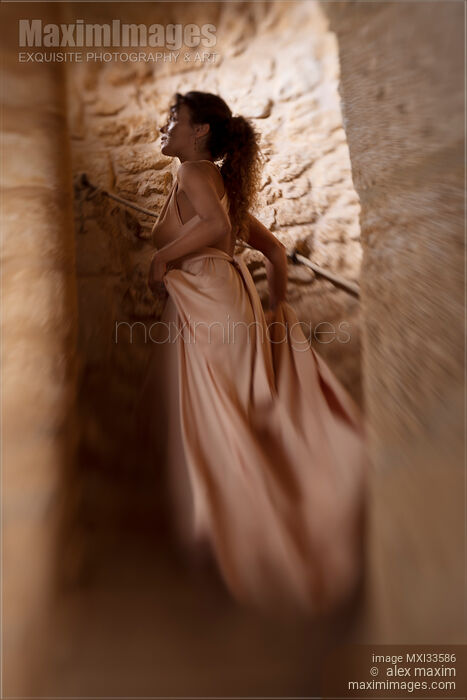 Stock photo of Woman in long dress running up the stairs of a spiral staircase in a dungeon of a medieval stone castle Buy commercial use license at MaximImages