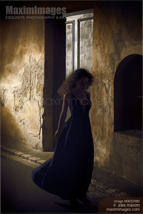 Stock photo of Woman in long dress walking along a shabby dark old street of European town at night Dramatic portrait France Buy commercial use license at MaximImages