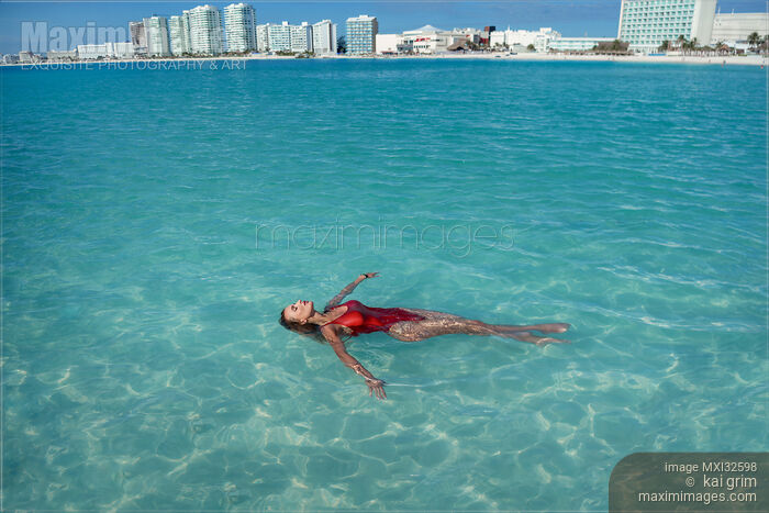 Woman in red swimsuit lying in clear blue water of Caribbean Sea with Cancun city skyline in the background Stock photo of Woman in red swimsuit lying in clear blue water of Caribbean Sea with Cancun city skyline in the background Buy commercial use license at MaximImages
