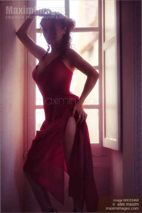 Stock photo of Woman in sexy elegant red dress standing by a bright French window in a seductive pose Buy commercial use license at MaximImages