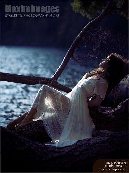 Woman in sheer white lace dress reclining against a tree by the lake in the nature at night in moonlight Stock photo of Woman in sheer white lace dress reclining against a tree by the lake in the nature at night in moonlight Buy commercial use license at MaximImages