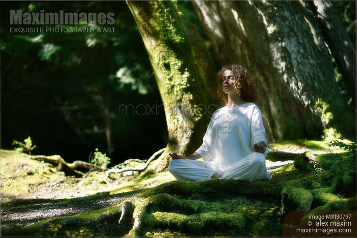 Stock photo of Woman in white clothes meditating in the nature in a deep green forest Buy commercial use license at MaximImages