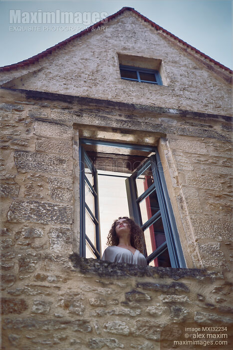 Woman looking out of an open window of an old French stone house Stock photo of Woman looking out of an open window of an old French stone house Buy commercial use license at MaximImages