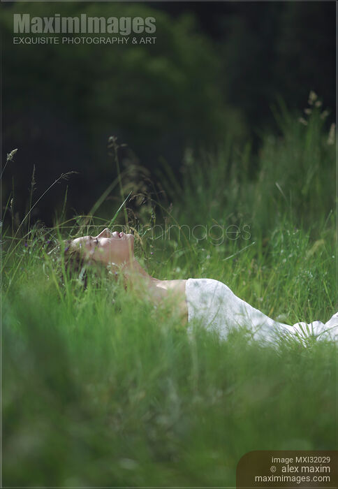 Stock photo of Woman lying in green grass with closed eyes in a sunny summer nature scenery Buy commercial use license at MaximImages
