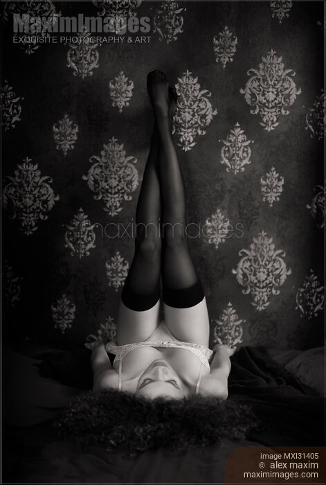 Stock photo of Woman lying on a bed in lingerie with sexy long legs in stockings up against the wall Black and white Buy commercial use license at MaximImages