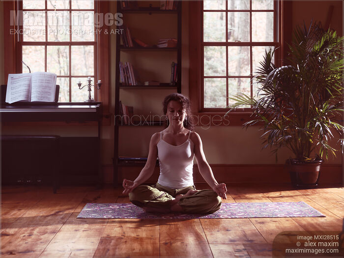 Stock photo of Woman meditating at home in dramatic dim light Buy commercial use license at MaximImages