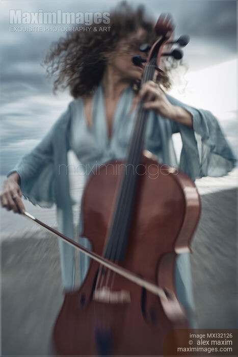Stock photo of Woman passionately playing cello on ocean shore with her hair flying in the wind Buy commercial use license at MaximImages