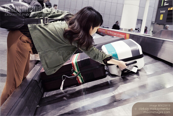Woman picking up suitcase from airport baggage claim conveyor Stock photo of Woman picking up suitcase from airport baggage claim conveyor Buy commercial use license at MaximImages