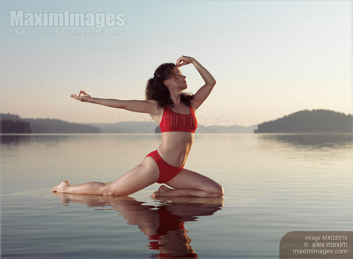 Stock photo of Woman practicing yoga on platform in the water doing Pigeon pose variation Buy commercial use license at MaximImages