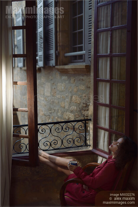 Woman resting in a chair by an open windows in France holding a cup of coffee in her hand Stock photo of Woman resting in a chair by an open windows in France holding a cup of coffee in her hand Buy commercial use license at MaximImages