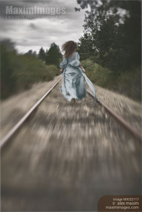 Woman running away along railroad tracks in a long dress flying in the wind Stock photo of Woman running away along railroad tracks in a long dress flying in the wind Buy commercial use license at MaximImages