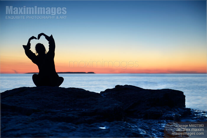 Stock photo of Woman silhouette alone on shore with hand in shape of flower Buy commercial use license at MaximImages
