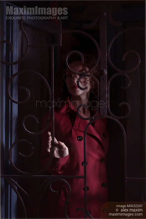 Woman standing behind locked grates touching the metal bars in a dark room Stock photo of Woman standing behind locked grates touching the metal bars in a dark room Buy commercial use license at MaximImages