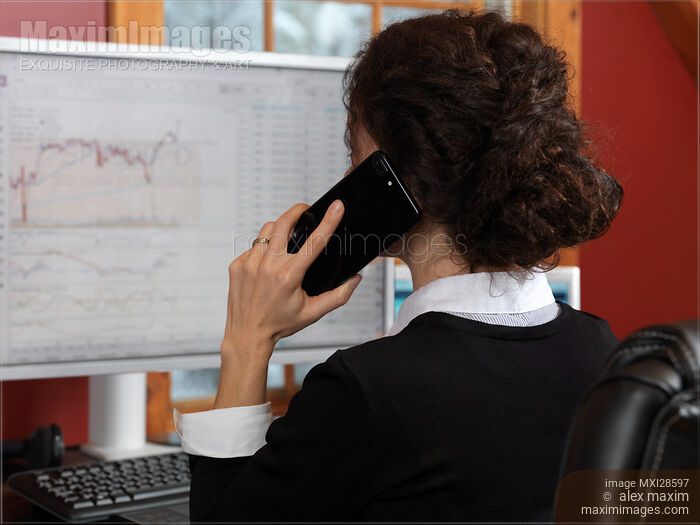 Stock photo of Woman stock trader speaking on the phone at a computer Buy commercial use license at MaximImages