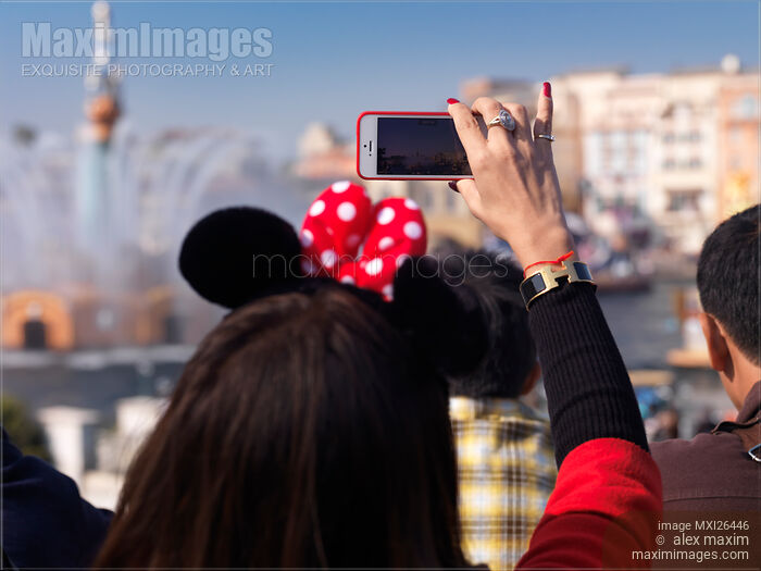 Woman taking pictures with iPhone of show at Tokyo Disneysea Stock photo of Woman taking pictures with iPhone of show at Tokyo Disneysea Buy commercial use license at MaximImages