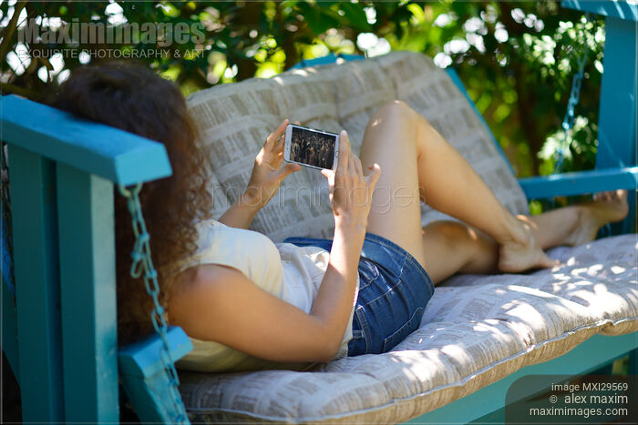 Stock photo of Woman watching video on iPhone smartphone screen outdoors Buy commercial use license at MaximImages