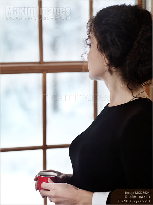 Woman with a cup of coffee standing by the window in winter Stock photo of Woman with a cup of coffee standing by the window in winter Buy commercial use license at MaximImages
